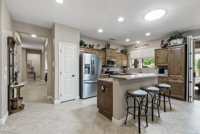 kitchen with a kitchen island, appliances with stainless steel finishes, tasteful backsplash, and a kitchen bar