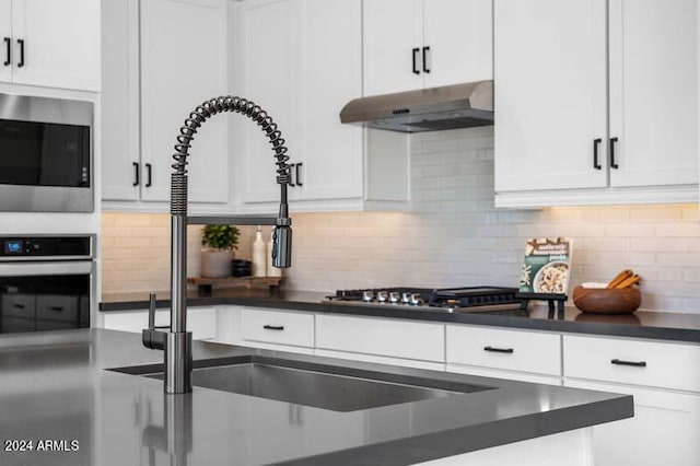 kitchen with appliances with stainless steel finishes, white cabinetry, backsplash, and range hood