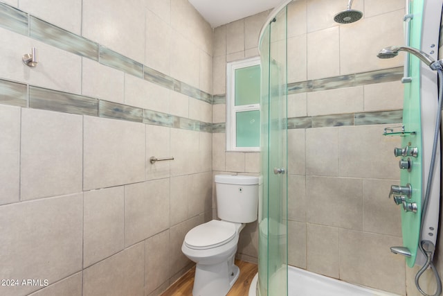 bathroom with tile walls, toilet, a shower with door, and wood-type flooring