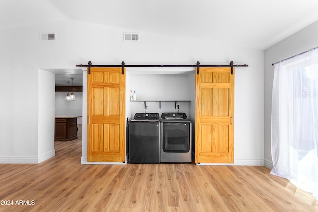 interior space featuring lofted ceiling, washing machine and clothes dryer, a barn door, and light hardwood / wood-style floors