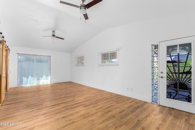 interior space with a barn door, ceiling fan, lofted ceiling, and light hardwood / wood-style floors