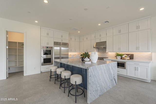 12326 E Black Rock Rd, Scottsdale, AZ 85255 - kitchen with a kitchen bar, tasteful backsplash, white cabinets, under cabinet range hood, and built in appliances