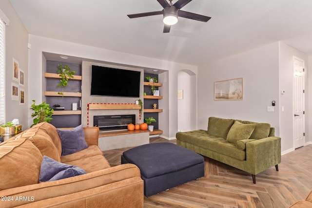 living area featuring baseboards, arched walkways, built in features, a glass covered fireplace, and ceiling fan