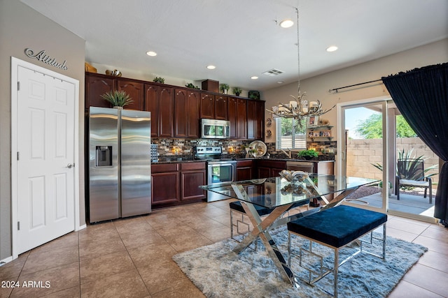 kitchen with appliances with stainless steel finishes, hanging light fixtures, tasteful backsplash, light tile patterned floors, and an inviting chandelier