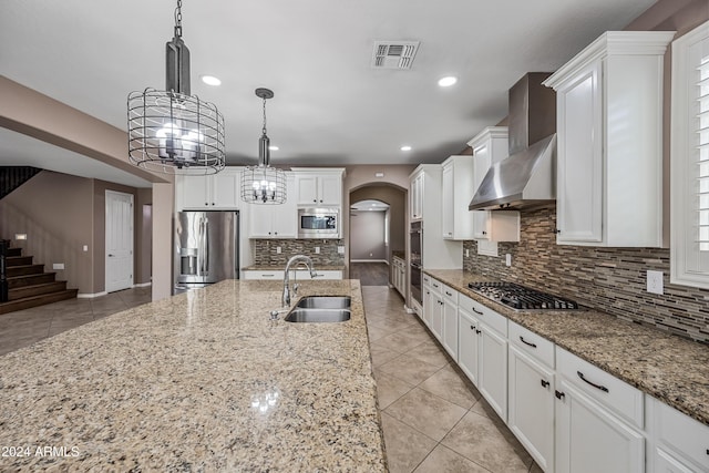 kitchen with sink, stainless steel appliances, wall chimney range hood, pendant lighting, and white cabinets