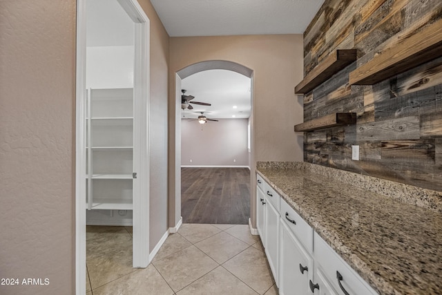 bar featuring light stone countertops, ceiling fan, wooden walls, light tile patterned floors, and white cabinets