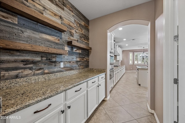 kitchen with white cabinets, pendant lighting, light stone counters, and wood walls