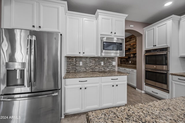 kitchen featuring light stone counters, white cabinetry, backsplash, and appliances with stainless steel finishes