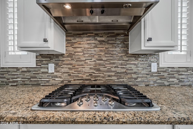 kitchen featuring stainless steel gas stovetop, white cabinetry, decorative backsplash, and range hood