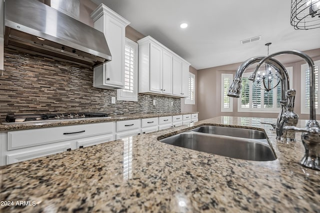 kitchen featuring sink, wall chimney range hood, stone counters, white cabinetry, and stainless steel gas stovetop