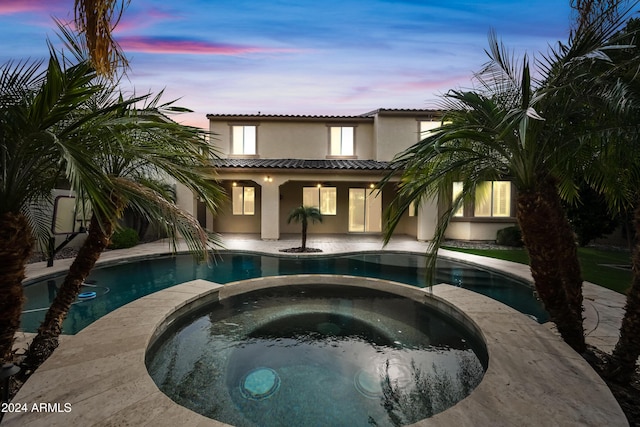 back house at dusk featuring a swimming pool with hot tub