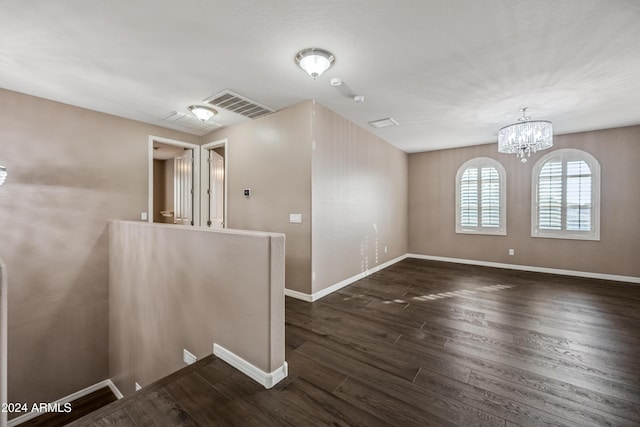 spare room with dark hardwood / wood-style floors and an inviting chandelier