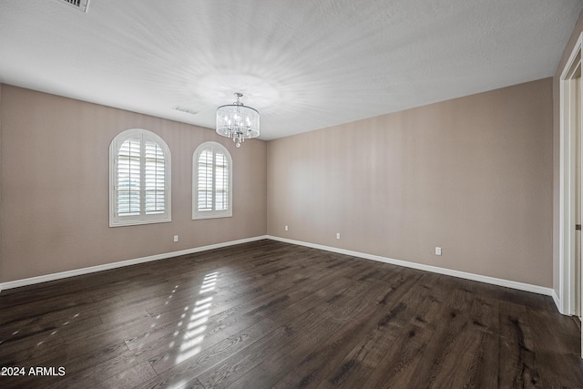 empty room featuring a notable chandelier and dark wood-type flooring