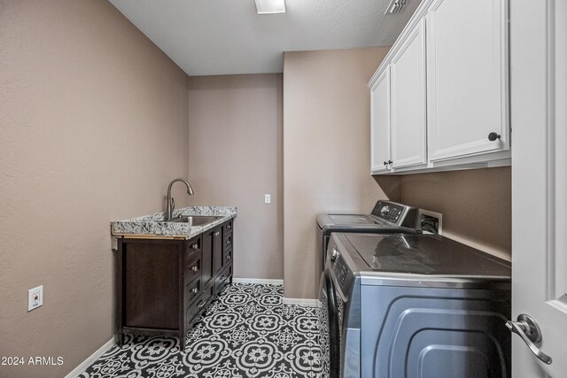 clothes washing area with washing machine and clothes dryer, sink, cabinets, and a textured ceiling