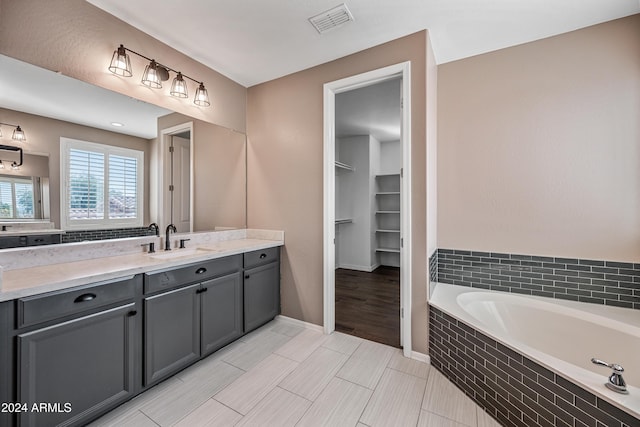 bathroom with wood-type flooring, vanity, and tiled bath