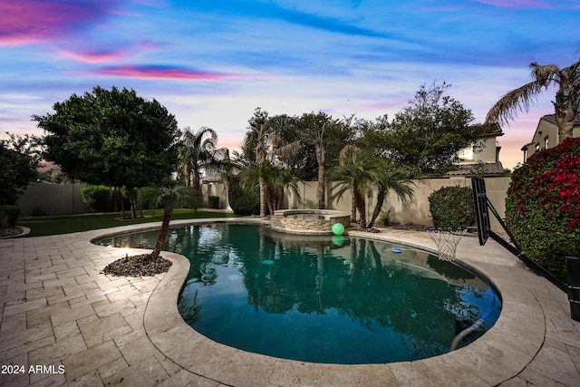 pool at dusk with an in ground hot tub and a patio