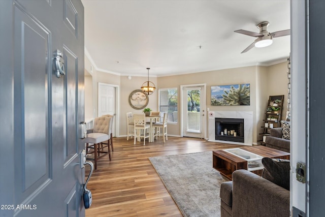 living area with light wood finished floors, baseboards, a ceiling fan, crown molding, and a fireplace