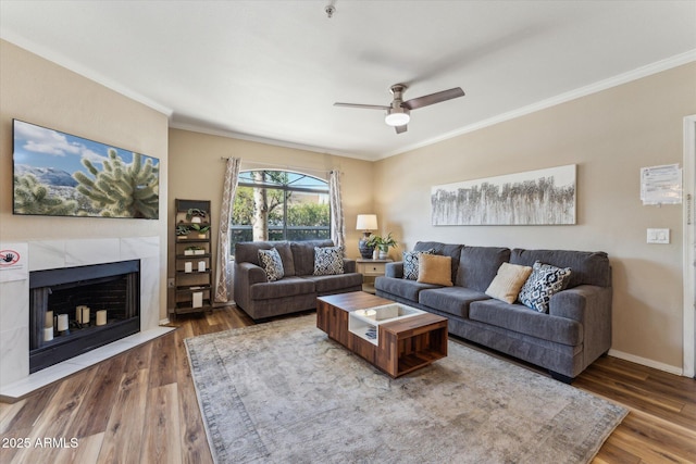 living room featuring ornamental molding, a fireplace, baseboards, and wood finished floors