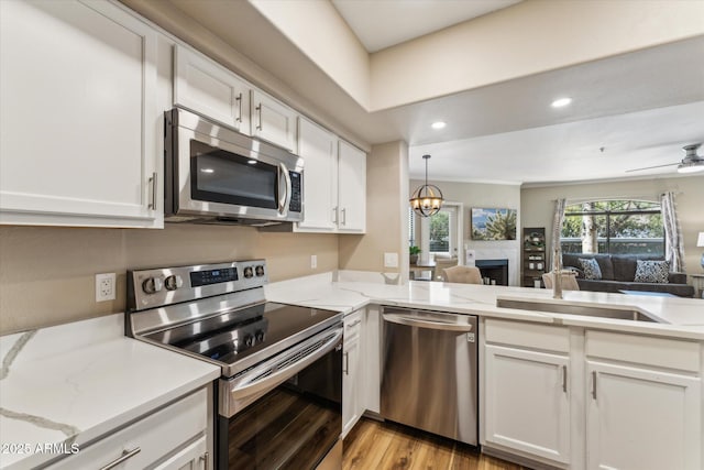 kitchen featuring light wood finished floors, white cabinets, appliances with stainless steel finishes, open floor plan, and ceiling fan with notable chandelier