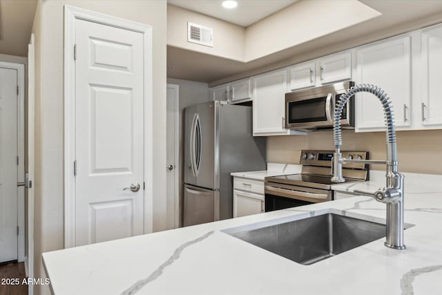 kitchen with appliances with stainless steel finishes, light stone countertops, visible vents, and white cabinetry