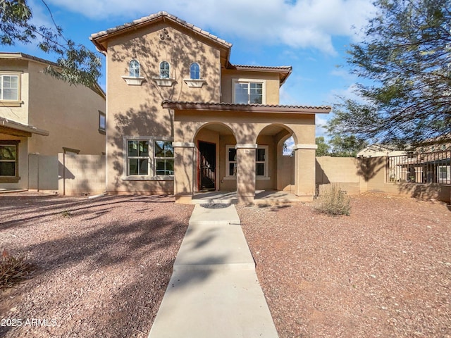 mediterranean / spanish-style home with a porch, a tile roof, fence, and stucco siding