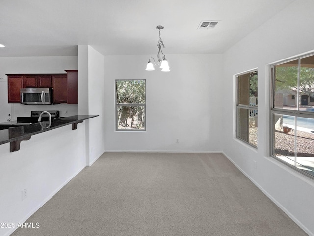 kitchen featuring light colored carpet, dark countertops, stainless steel microwave, a breakfast bar area, and dark brown cabinets