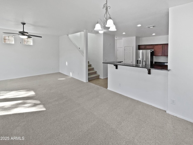 unfurnished living room with stairs, recessed lighting, light colored carpet, visible vents, and ceiling fan with notable chandelier