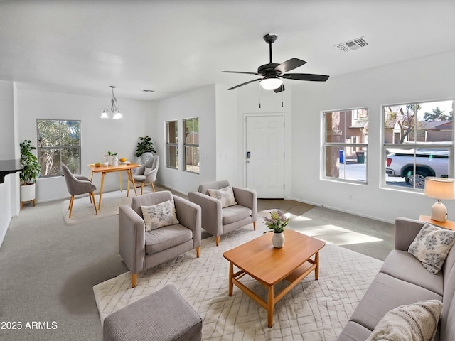 living room featuring baseboards, ceiling fan with notable chandelier, visible vents, and light colored carpet