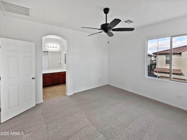 unfurnished bedroom with baseboards, visible vents, arched walkways, light colored carpet, and ensuite bathroom