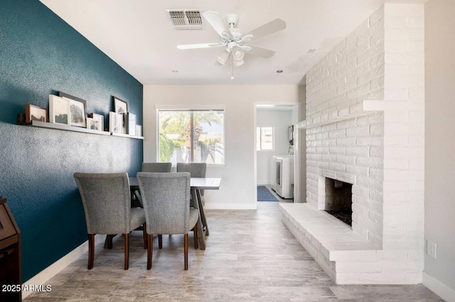 dining area featuring a brick fireplace, light hardwood / wood-style flooring, washer / clothes dryer, and ceiling fan