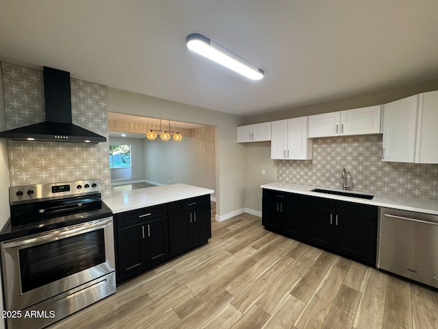 kitchen with dark cabinets, stainless steel appliances, a sink, white cabinetry, and wall chimney exhaust hood