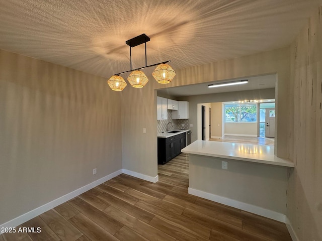 kitchen featuring dark wood-style flooring, decorative light fixtures, light countertops, white cabinetry, and a sink