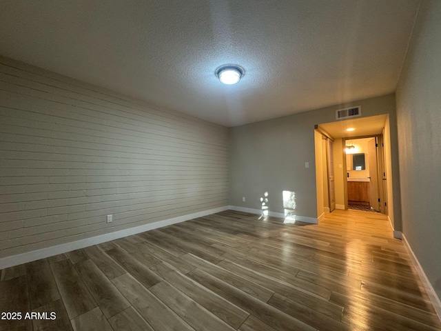 spare room with a textured ceiling, wood finished floors, and baseboards