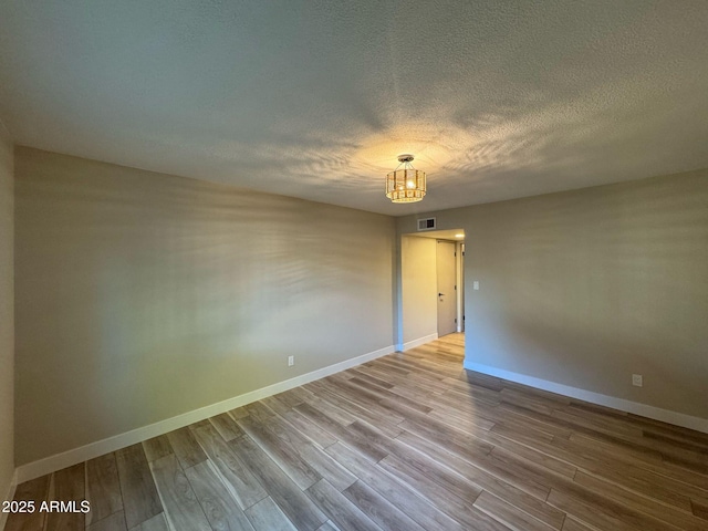 empty room with a textured ceiling, wood finished floors, visible vents, and baseboards