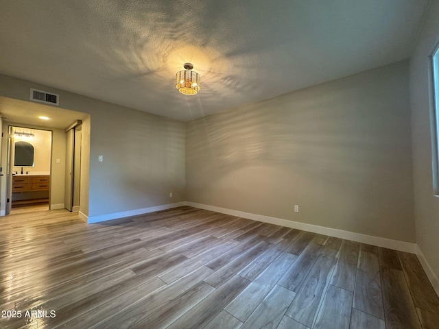 empty room with visible vents, a textured ceiling, baseboards, and wood finished floors