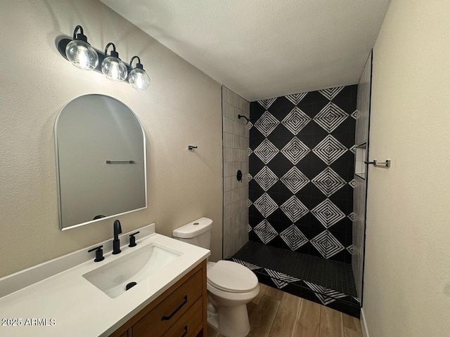 full bathroom featuring a tile shower, vanity, toilet, and wood finished floors