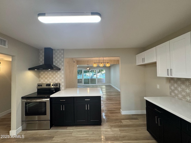 kitchen with light countertops, dark cabinetry, backsplash, stainless steel electric range oven, and wall chimney exhaust hood