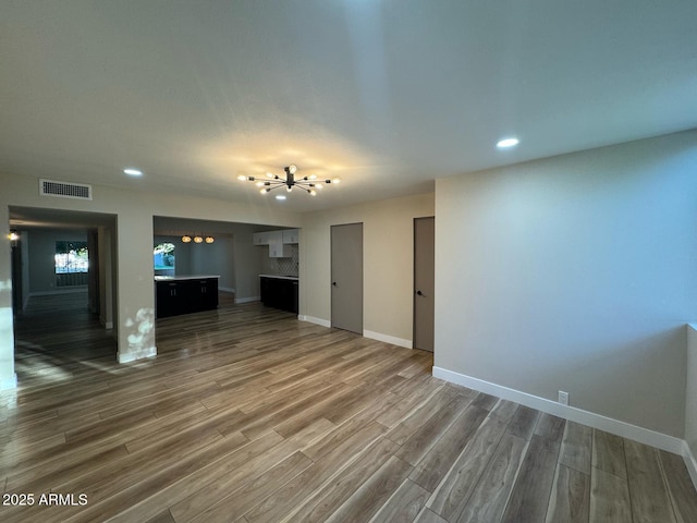 unfurnished living room featuring dark wood-style floors, a notable chandelier, recessed lighting, visible vents, and baseboards