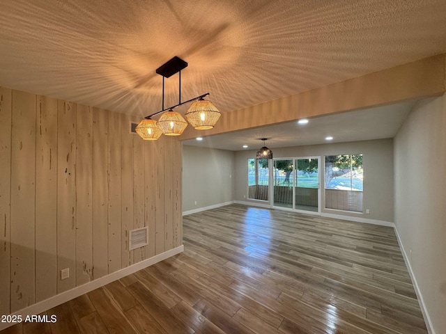 spare room with wood walls, baseboards, visible vents, and wood finished floors