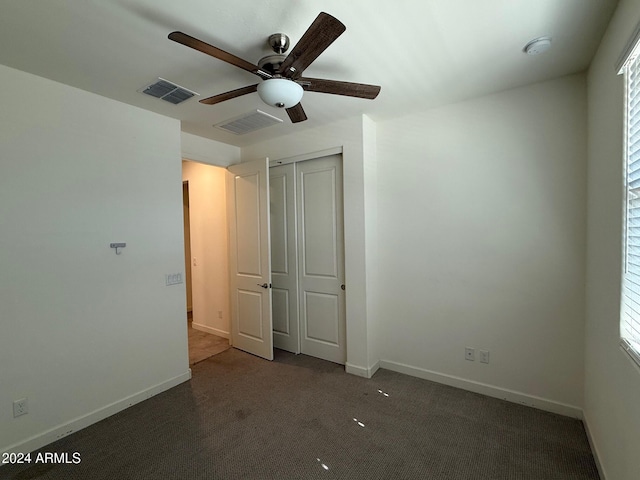 unfurnished bedroom with dark colored carpet, ceiling fan, a closet, and multiple windows