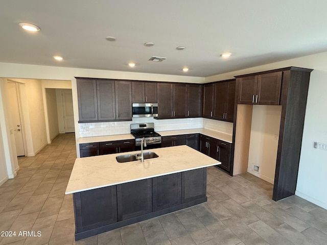 kitchen featuring a center island with sink, sink, decorative backsplash, dark brown cabinets, and stainless steel appliances