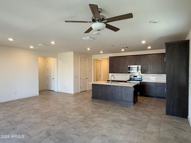 kitchen with appliances with stainless steel finishes, backsplash, ceiling fan, sink, and an island with sink