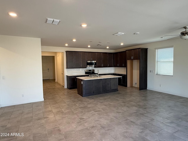 kitchen with appliances with stainless steel finishes, dark brown cabinetry, a center island with sink, and ceiling fan