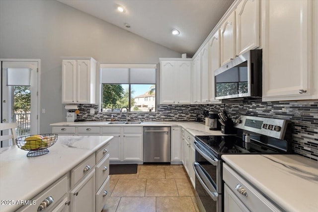 kitchen with sink, white cabinets, vaulted ceiling, light tile patterned floors, and appliances with stainless steel finishes