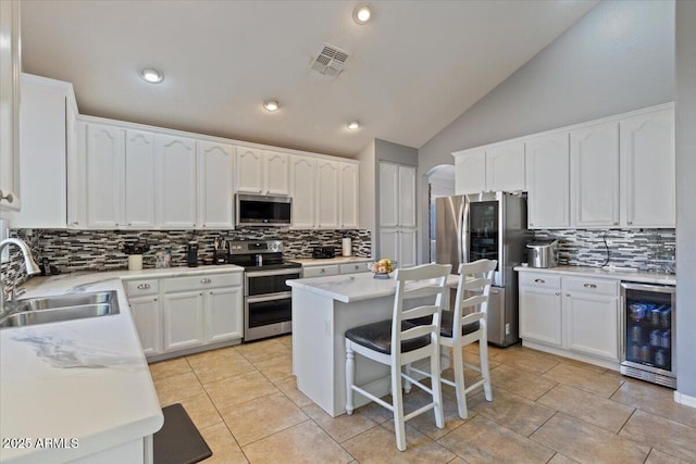 kitchen featuring stainless steel appliances, sink, a center island, lofted ceiling, and beverage cooler