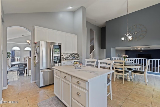 kitchen featuring a center island, stainless steel fridge, white cabinetry, decorative light fixtures, and tasteful backsplash