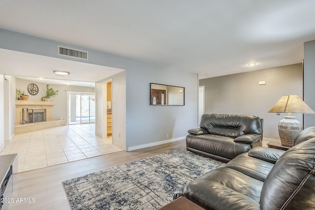 living room featuring light wood-style floors, visible vents, a fireplace, and baseboards