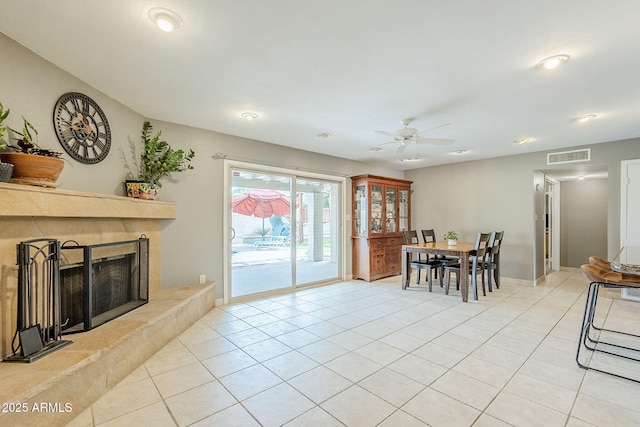 interior space featuring light tile patterned flooring, a tile fireplace, a ceiling fan, visible vents, and baseboards