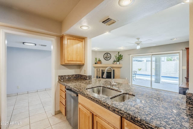 kitchen featuring visible vents, dishwasher, dark stone countertops, light brown cabinets, and a sink