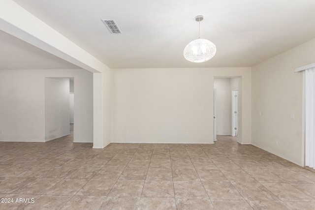 tiled spare room featuring a notable chandelier